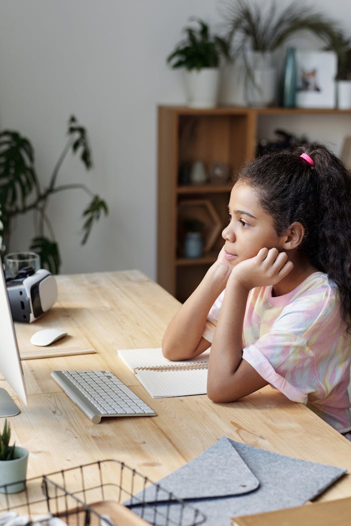 Services Girl studying online at home, concentrating on computer screen with hands on cheeks.