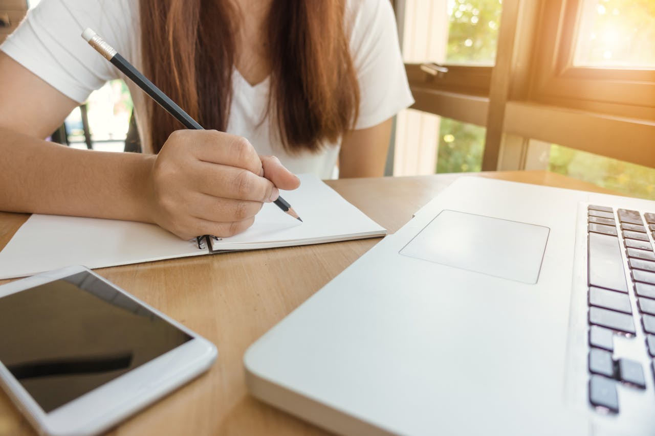 Mastering the First Impression: Your intriguing post title goes here A young woman writing notes at a table with laptop and smartphone.